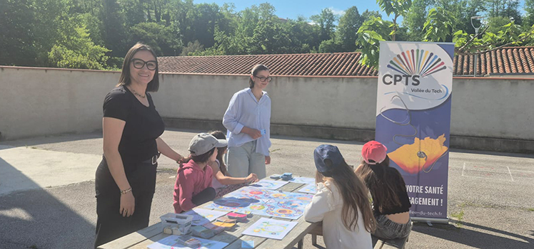 Deux professionnelles de la CPTS Vallée du Tech animent un atelier pédagogique en plein air, où des enfants participent à des activités de sensibilisation à la santé autour d'une table.