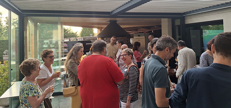 Groupe de personnes discutant lors d'un cocktail convivial dans un espace de réception moderne avec de grandes baies vitrées ouvertes sur un jardin.