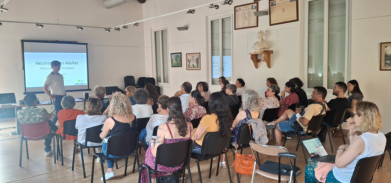 Professionnel de santé présentant une conférence sur la vaccination des adultes et les nouveaux rattrapages vaccinaux devant une assemblée de participants dans une salle municipale à Céret.